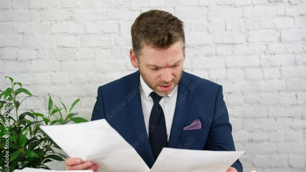 A stressed and confused busy businessman is looking at paperwork and his large work load at a desk in an office. A stressed and confused busy businessman is looking at paperwork and his large work load at a desk in an office.