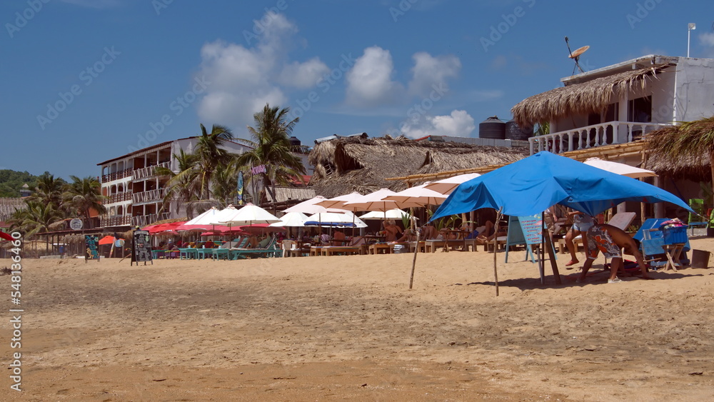Colorful umbrellas in front of tropical beach resort structures with thatched roofs in Zipolite, Mexico