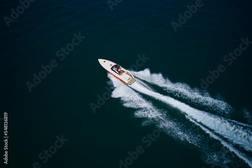 High-performance white-orange boat with people moving fast on dark blue water leave a white trail, top and top