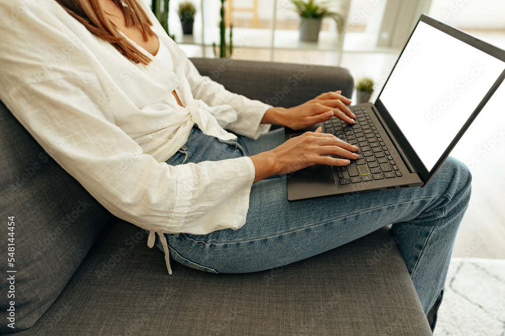 Naklejka premium Woman using laptop computer while sitting on a sofa at home.