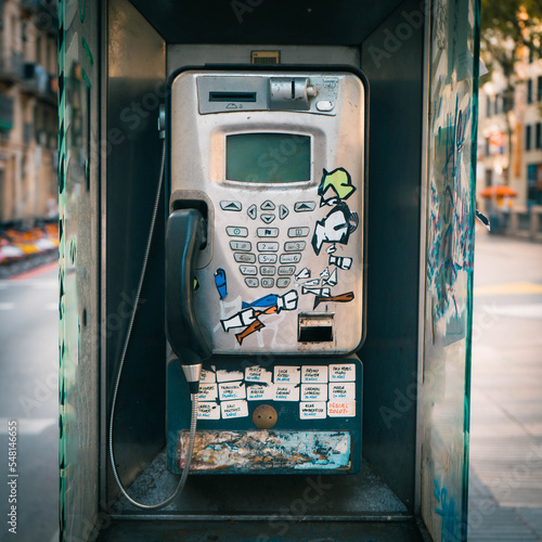 Telephone box in an urban environment in bad condition due to graffitis and stickers