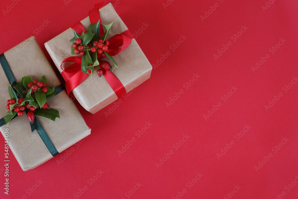 Two Christmas gifts with Holly decoration with red berries on a red background with copy space