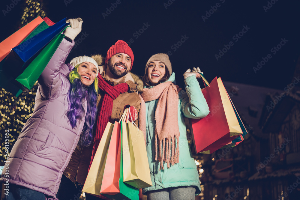 Fototapeta premium Photo of three excited positive people hold shopping packages have good mood tree garland outside