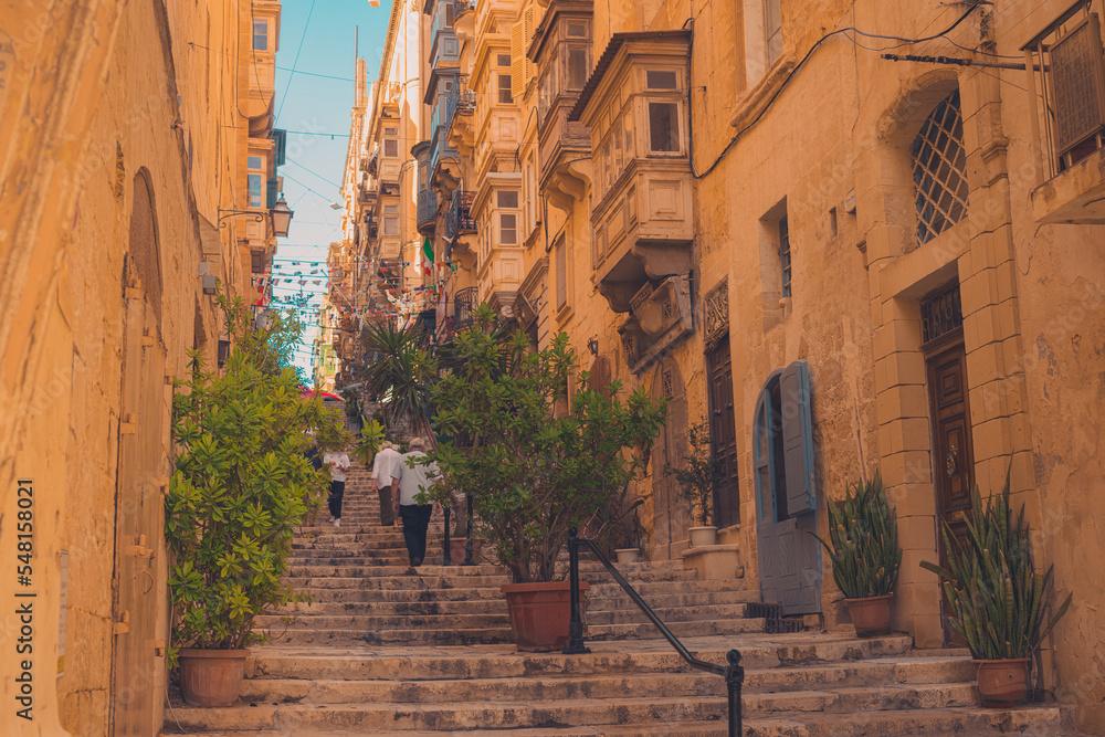 Picturesque streets and alleys of Valletta, Malta on summer sun. Visible long stairs and people walking on them.