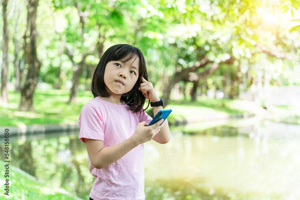 Beautiful asian child girl using mobile smartphone. Little girl is playing in digital game in the green park. Beautiful asian child girl using mobile smartphone. Little girl is playing in digital game in the green park.
