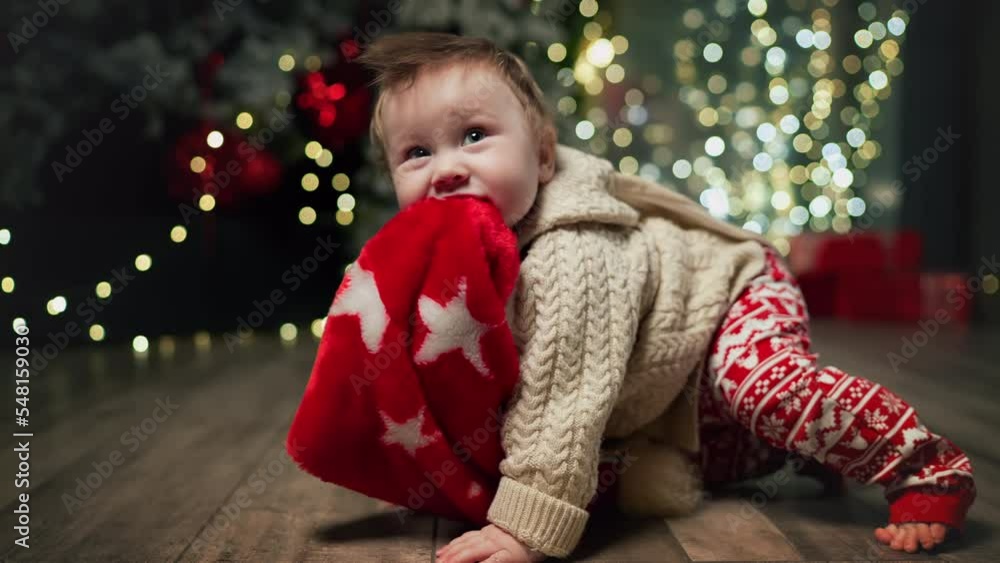 child in Santa Claus hat crawl on knees by Christmas fireplace. Kid sit down by Christmas fireplace and looks into camera. Funny boy celebrates Merry Christmas, happy new year toddler loving parents child in Santa Claus hat crawl on knees by Christmas fireplace. Kid sit down by Christmas fireplace and looks into camera. Funny boy celebrates Merry Christmas, happy new year toddler loving parents