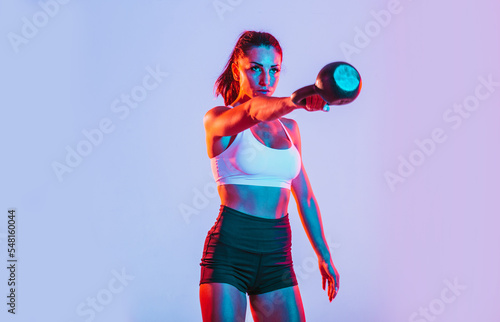 Artistic image with colored gel lights of a beautiful fit woman making exercises in the gym with sport equipments and gear