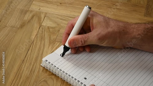A person is thinking ahead to the coming year by sitting down and writing by hand his goals for2023 written with a black marker on a lined writing pad.