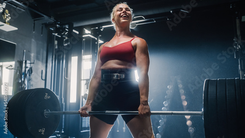 A Determined Sportswoman Exercising, Professionally Lifting Weights and Celebrating Her Achievement in Dark Gym. An Uncompromising Woman Training, Smiles After Finishing her Workout