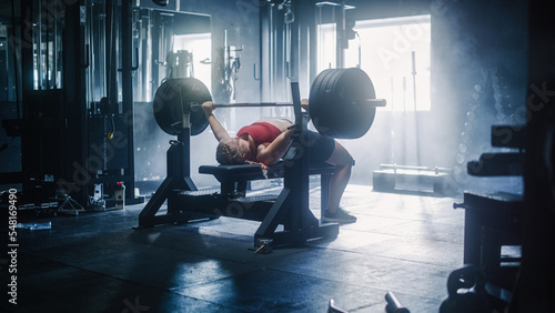 Professional Female Athlete Doing Bench Press Workout Using Barbell In a Grunge Hardcore Gym. An Inspiring Bodybuilder Training and Exercising with Heavy Weights In a Deserted Gym. Wide Shot photo