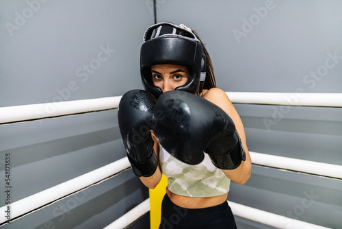 Foto Woman with protective gloves and headgear in attack position on a ring boxing