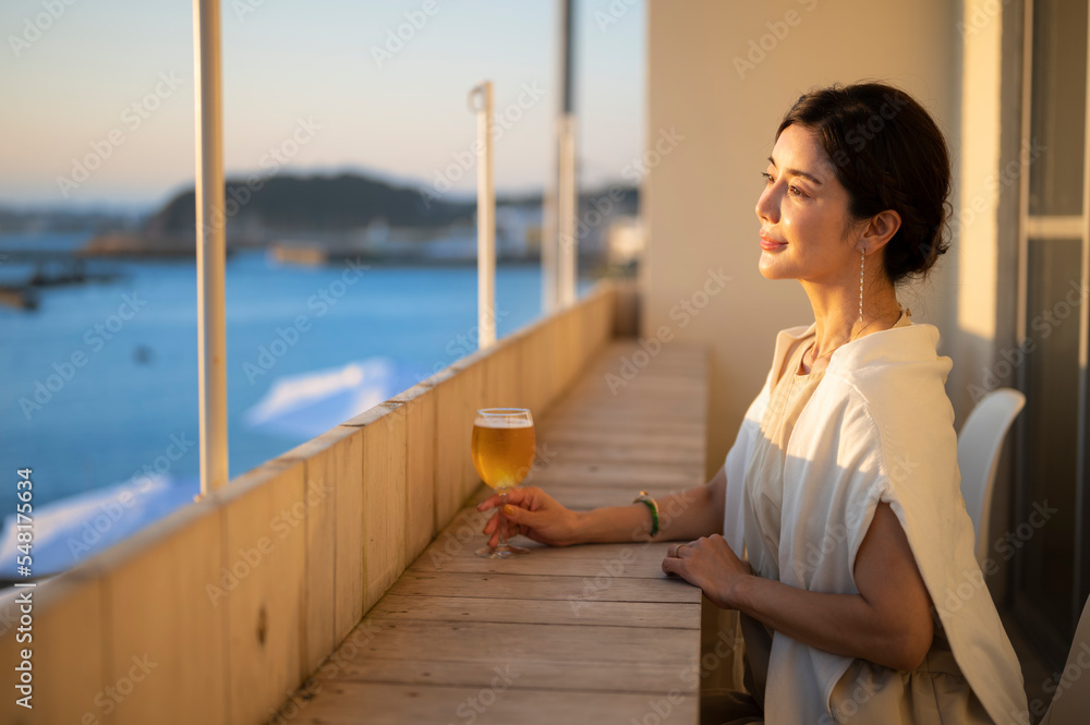 サンセットが美しい海辺のカフェでビールを飲む女性