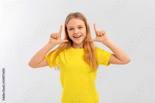 Enthusiastic teen girl pointing fingers up, looking surprised and amazed by company banner, standing in casual yellow t shirt over white background