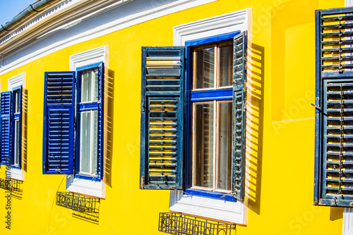 Traditional windowed building in Sibiu town Romania. Saxon house with yellow wall and blue window blinds.