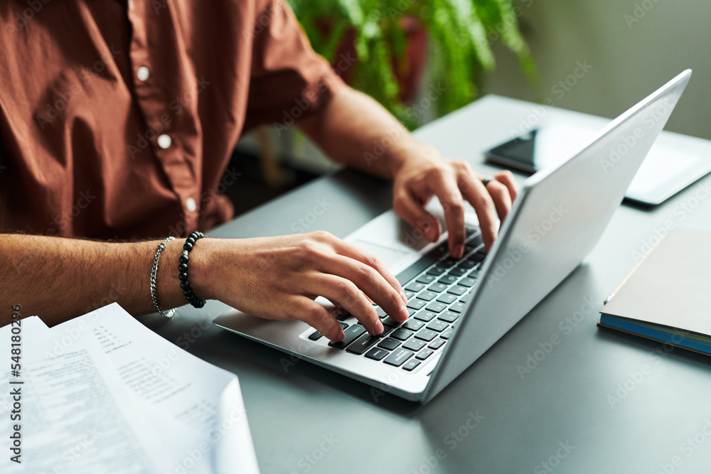 Close-up of hands of young student typing on laptop keyboard while sitting by workplace and carrying out online grammar test Close-up of hands of young student typing on laptop keyboard while sitting by workplace and carrying out online grammar test