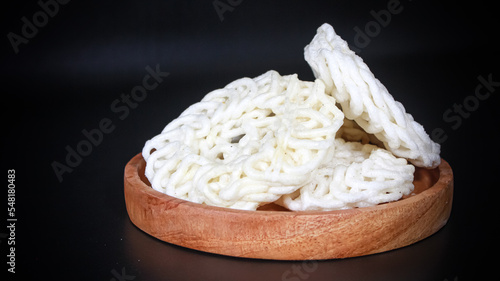 Krupuk Uyel or Kerupuk Uyel is one of type Indonesia traditional crackers. Served in wooden plate. Isolated on black background. Close up. photo