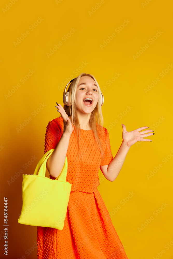 Astonished young beautiful emotional girl in orange dress dancing, smiling, having fun isolated over orange background. Vivid emotions, happiness, hobbies and joy Astonished young beautiful emotional girl in orange dress dancing, smiling, having fun isolated over orange background. Vivid emotions, happiness, hobbies and joy