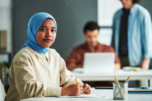 Foto Young Muslim woman in blue hijab looking at camera while lchecking or carrying o