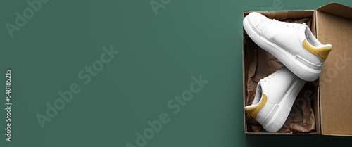 Cardboard box with stylish white shoes on green background with space for text