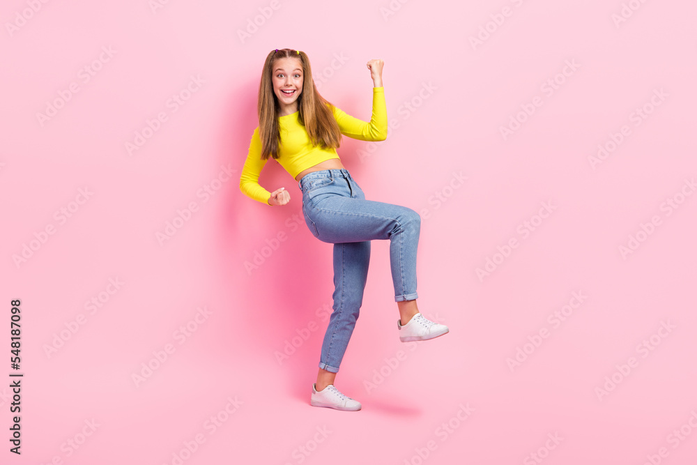 Full length photo of lucky excited school girl dressed yellow crop top walking rising fists isolated pink color background Full length photo of lucky excited school girl dressed yellow crop top walking rising fists isolated pink color background