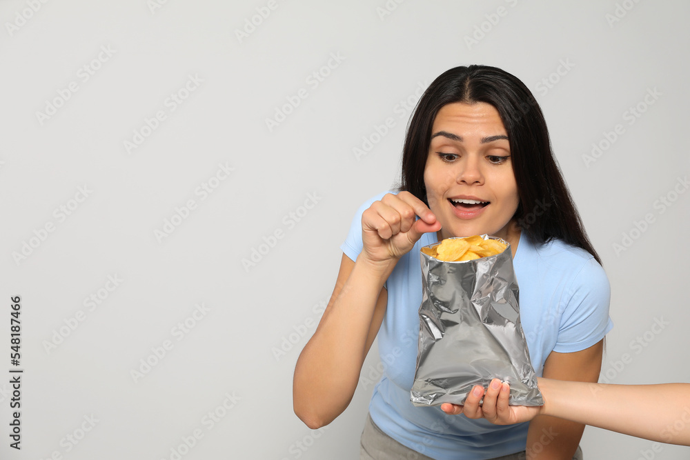 Beautiful young woman eating tasty potato chips on grey background, space for text Beautiful young woman eating tasty potato chips on grey background, space for text