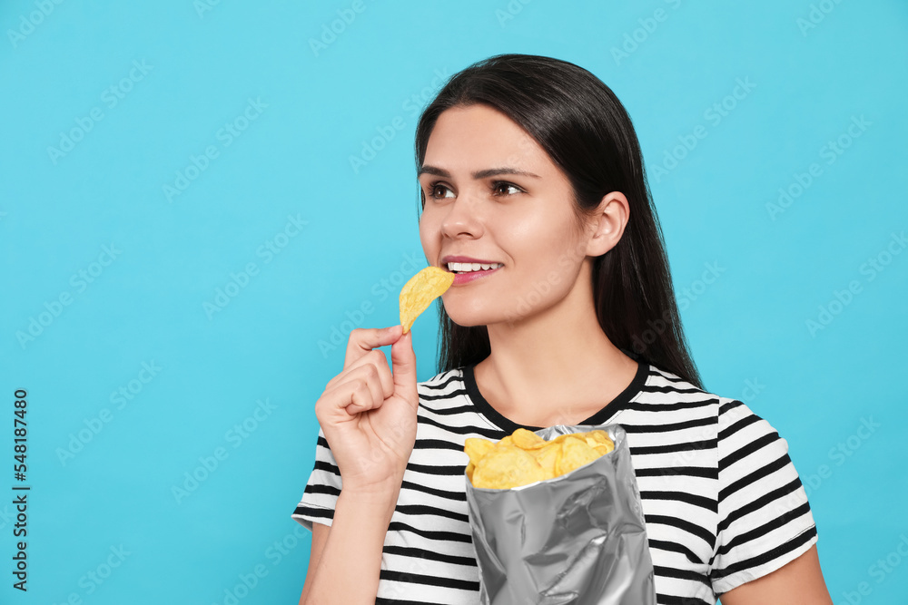 Beautiful woman eating potato chips on light blue background. Space for text Beautiful woman eating potato chips on light blue background. Space for text