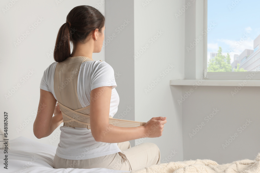 Woman with orthopedic corset sitting in bedroom, back view Woman with orthopedic corset sitting in bedroom, back view