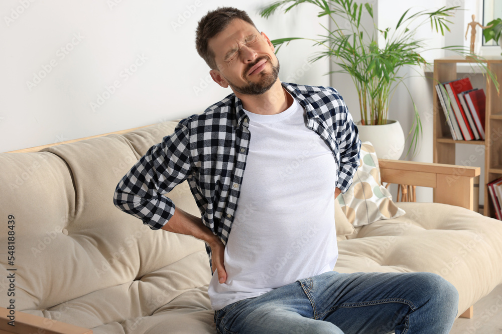 Man suffering from pain in back on sofa at home Man suffering from pain in back on sofa at home