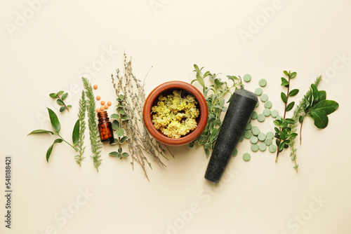 Composition with wooden mortar, pestle, pills and herbs on light background