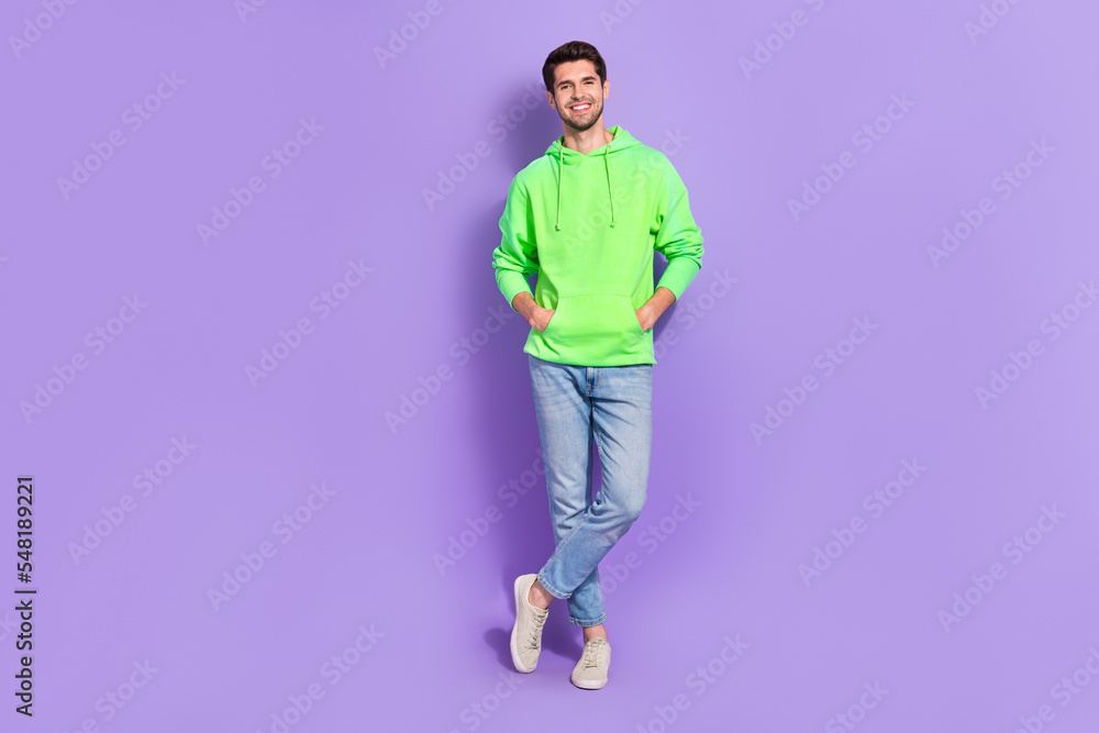 Fototapeta premium Full body size photo of attractive guy wear bright green hoodie stylish jeans confident empty space new brand isolated on purple color background