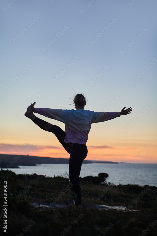 woman performing a complicated yoga position in nature at sunset with no recognizable face, vertical with copy space woman performing a complicated yoga position in nature at sunset with no recognizable face, vertical with copy space