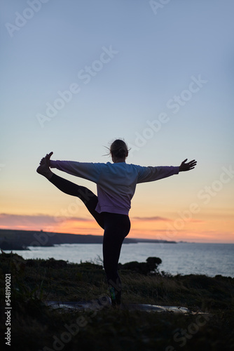 woman performing a complicated yoga position in nature at sunset with no recognizable face, vertical with copy space
