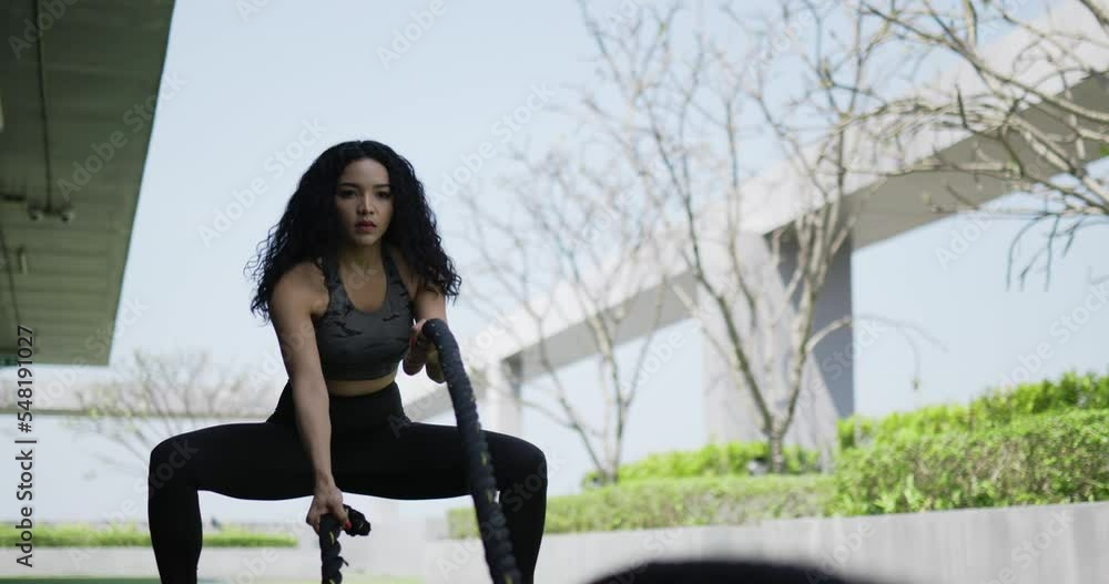 Handheld shot, Curly hair woman training her hands using rope crossfit exercise in Muscular fitness woman trains triceps program with two cables by her hands at outdoor of fitness center Handheld shot, Curly hair woman training her hands using rope crossfit exercise in Muscular fitness woman trains triceps program with two cables by her hands at outdoor of fitness center