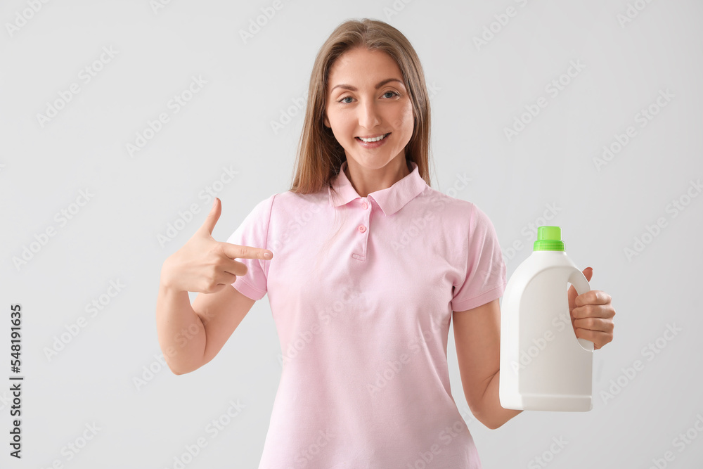 Young woman pointing at bottle of detergent on light background Young woman pointing at bottle of detergent on light background