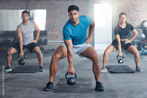 Fitness  kettlebell weight and people doing an exercise for strength  wellness or health together in a gym. Sports  motivation and athletes doing a squat workout with personal trainer in sport studio