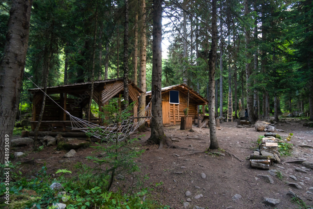 Wooden house hut with gazebo, hammock, a place to relax in the forest. Concept of tourists' rest, a halt. Beautiful atmospheric place in the forest for tourists Wooden house hut with gazebo, hammock, a place to relax in the forest. Concept of tourists' rest, a halt. Beautiful atmospheric place in the forest for tourists