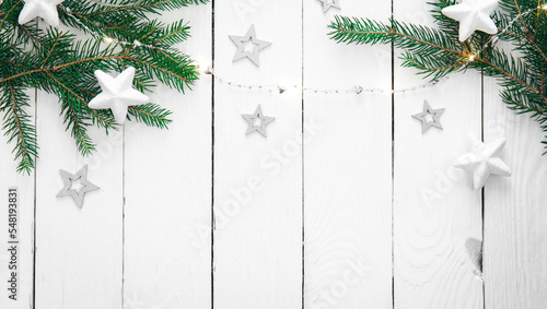 Wooden Christmas background with fir branches, garland and decorative stars.