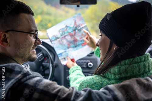 A man and lady holding and looking at paper map, sitting inside car.
