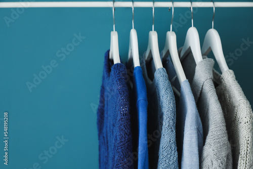 Rack with knitted sweaters near blue wall, closeup