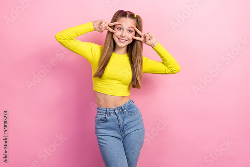 Portrait of optimistic girl with straight hair dressed yellow long sleeve showing v-sign near eyes isolated on yellow color background
