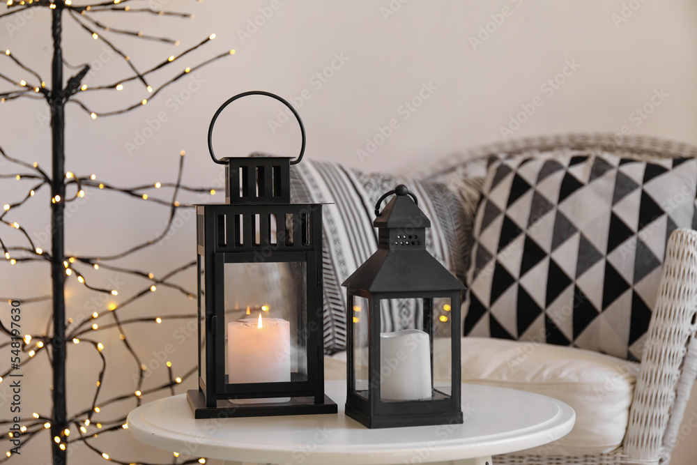 Black Christmas lanterns with burning candles on table in living room