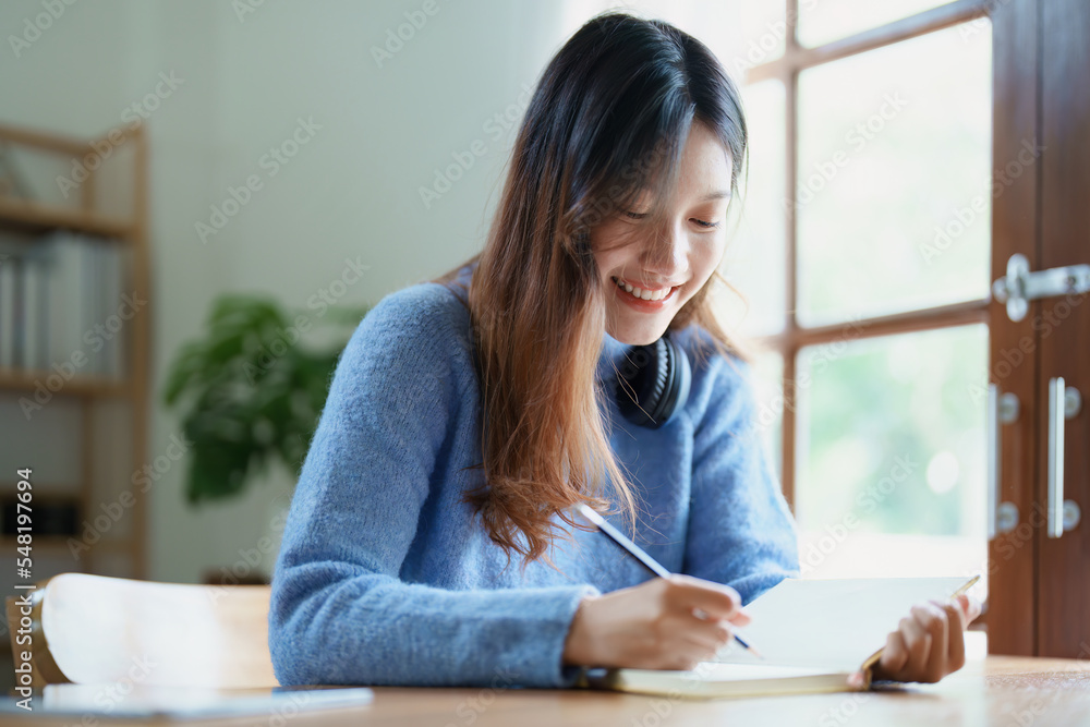 Portrait of a teenage Asian woman using a notebook to study online via video conferencing on a wooden desk at home Portrait of a teenage Asian woman using a notebook to study online via video conferencing on a wooden desk at home