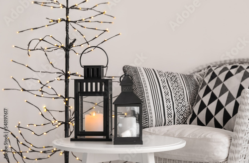 Black Christmas lanterns with burning candles on table in living room