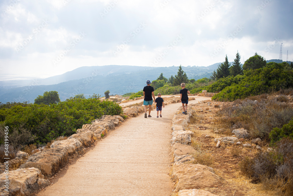 Man with child sitting on the edge of the mountain and showing the landscape to the kid. Hiking with family