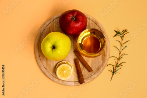 Wooden board with fresh apples, glass of juice and cinnamon sticks on color background