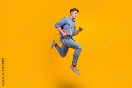 Full length photo of cheerful caucasian smart young man holding laptop smiling jumping high running on isolated bright background © Tetiana