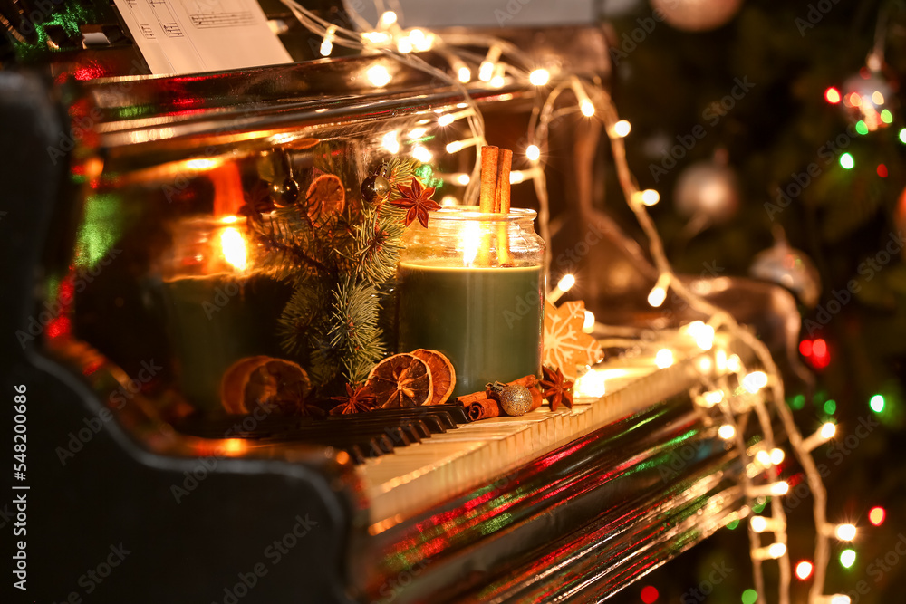 Burning candle with Christmas treats, decor and glowing lights on piano keys, closeup Burning candle with Christmas treats, decor and glowing lights on piano keys, closeup