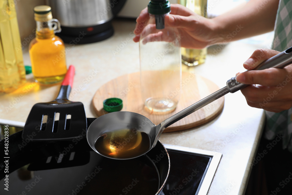Woman with used cooking oil and empty bottle near stove in kitchen, closeup Woman with used cooking oil and empty bottle near stove in kitchen, closeup