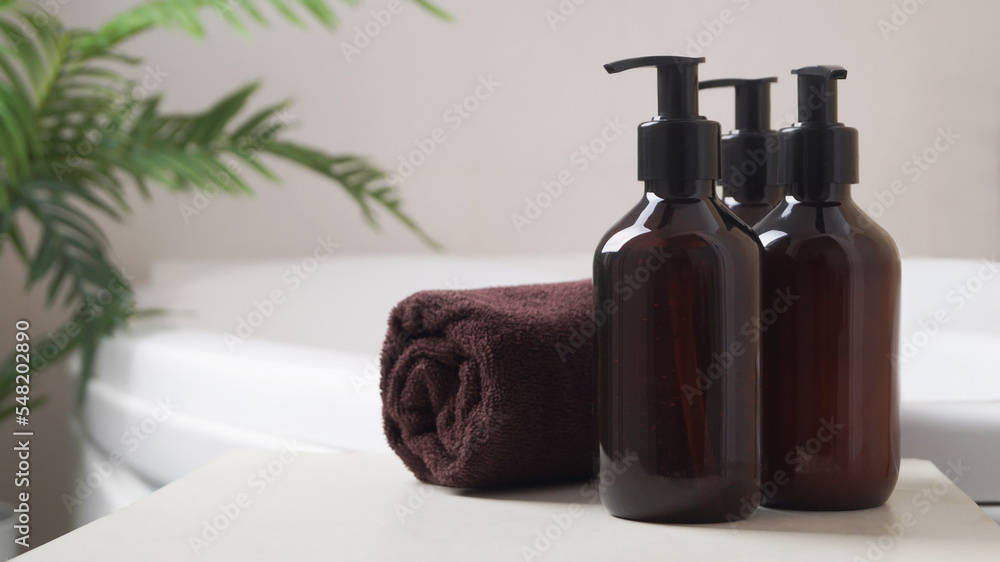 Bath foam and other personal hygiene products in bottles and rolled towel on small table in bathroom, space for text Bath foam and other personal hygiene products in bottles and rolled towel on small table in bathroom, space for text