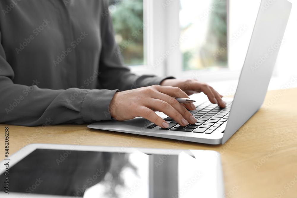 Woman with tablet and pen working on laptop at wooden table, closeup. Electronic document management Woman with tablet and pen working on laptop at wooden table, closeup. Electronic document management